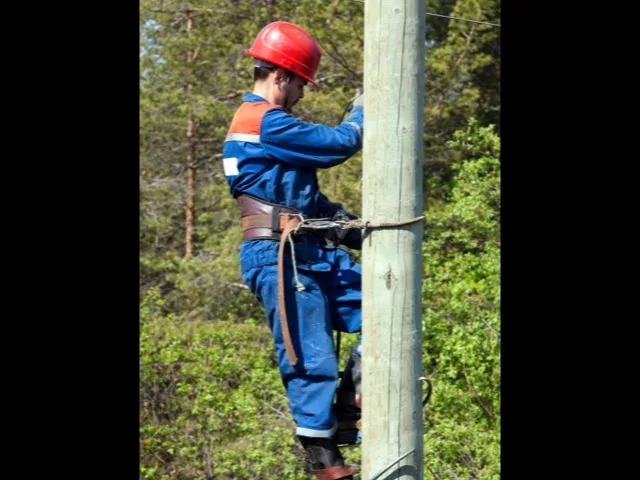 Szerelő teljes védőfelszerelésben, sisakban oszlopmunka közben